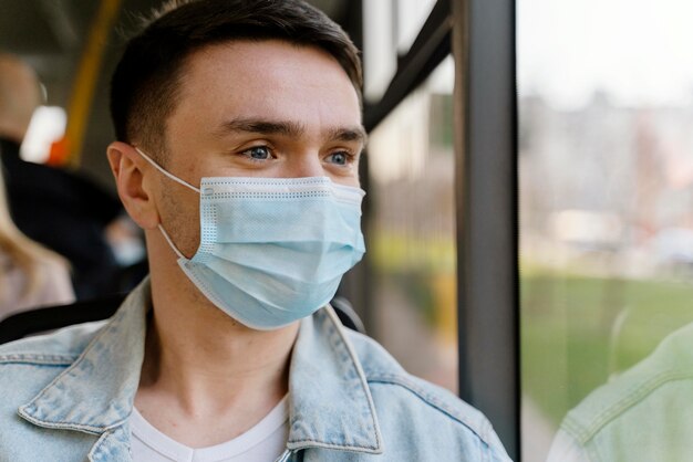 Young man travelling by city bus wearing surgical mask