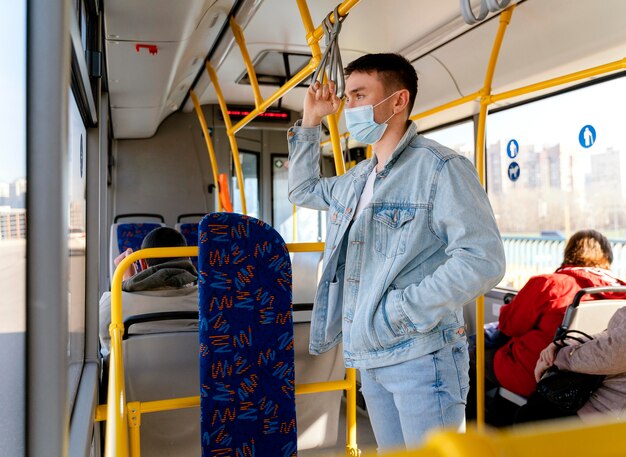 Young man travelling by city bus wearing surgical mask