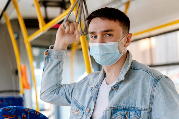 Young man travelling by city bus wearing surgical mask