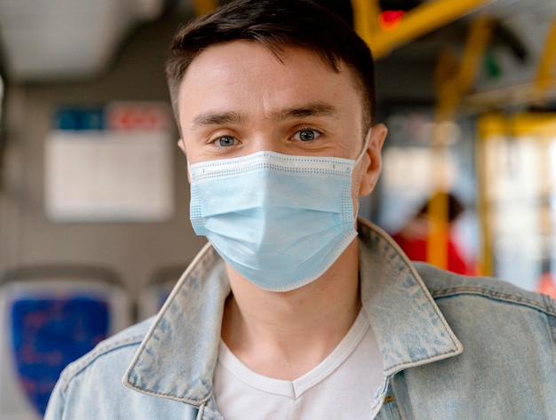 Young man travelling by city bus wearing surgical mask