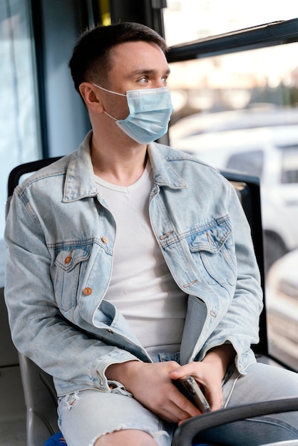 Free photo young man travelling by city bus wearing surgical mask