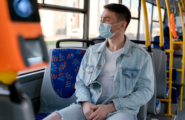 サージカルマスクを身に着けている市バスで旅行している若い男
