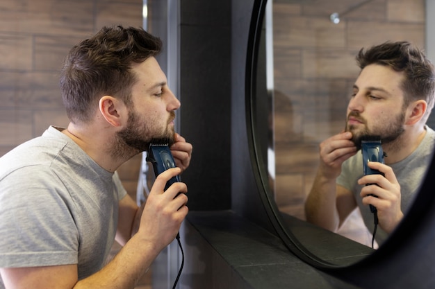 Young man trimming his beard in the mirror