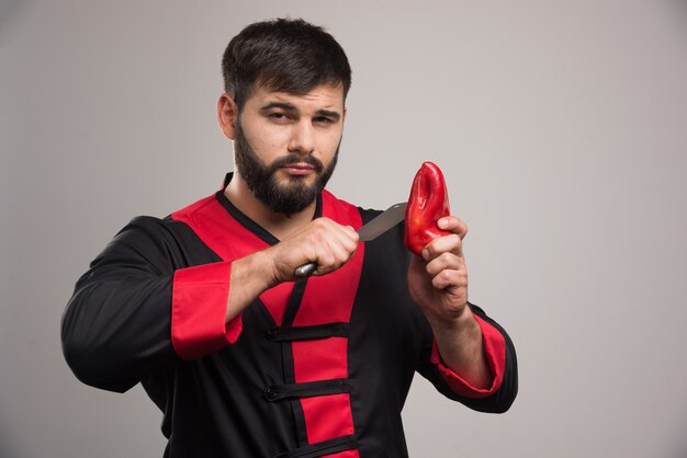 Young man trying to cut red pepper with knife .