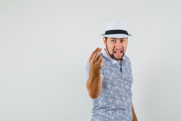 Young man trying to explain something while screaming in t-shirt, hat and looking furious. front view.