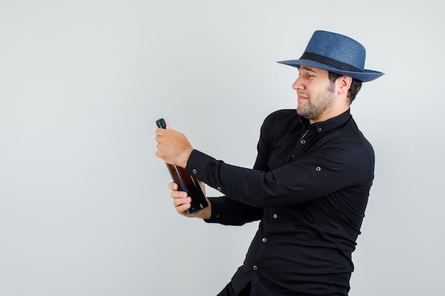 Free photo young man trying to open alcohol bottle in black shirt