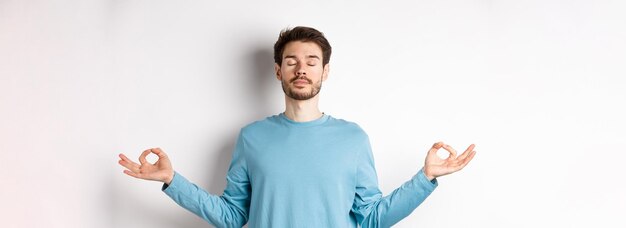 Young man trying to relax in meditation standing calm with stretch out hands in zen mudra gesture pr