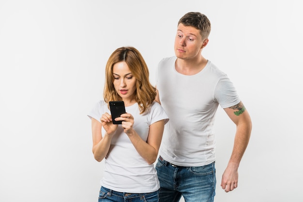 흰색 배경에 고립 된 그녀의 여자 친구의 휴대 전화를 스파이하려고하는 젊은 남자