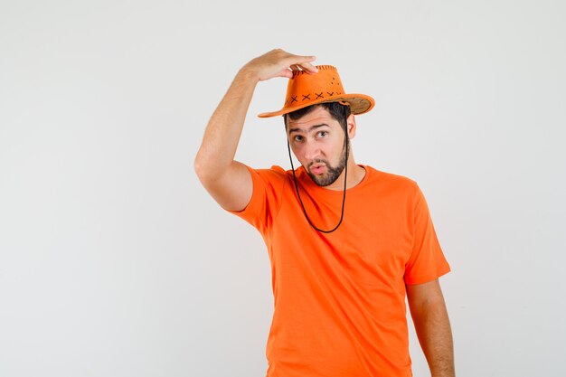 Young man trying to taking off his hat in orange t-shirt front view.