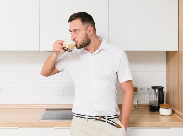 Молодой человек в футболке, попивая кофе на кухне