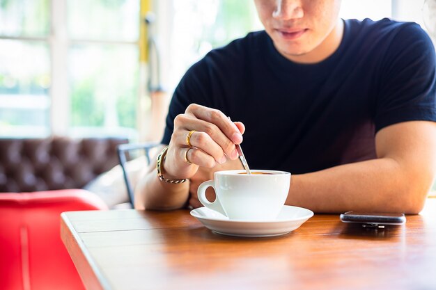 若い男はコーヒーカップに小さなスプーンを使う