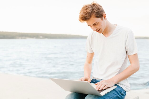 Young man using laptop by the water