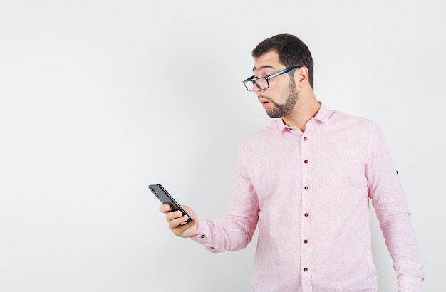 Free photo young man using mobile phone in pink shirt and looking focused