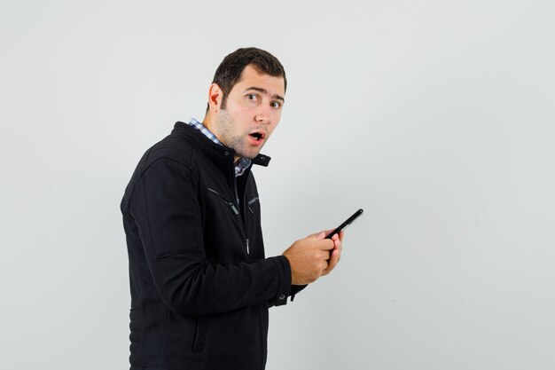 Young man using mobile phone in shirt, jacket and looking wondered. .