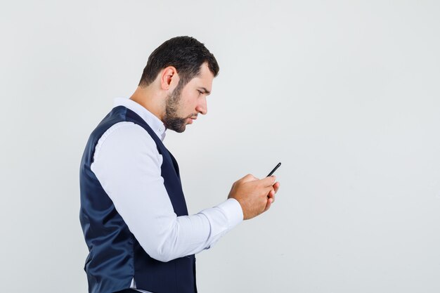 Young man using mobile phone in shirt and vest and looking busy .