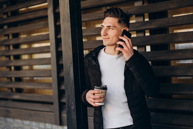 전화를 사용하고 거리에서 커피를 마시는 젊은 남자