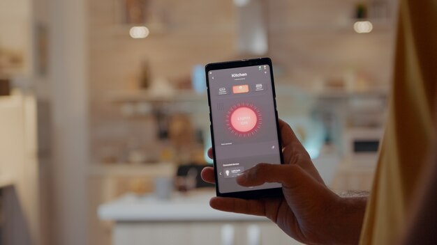 스마트 홈 응용 프로그램 소프트웨어 터치 스크린을 사용하여 젊은 남자가 휴대 전화로 빛을 켭니다.