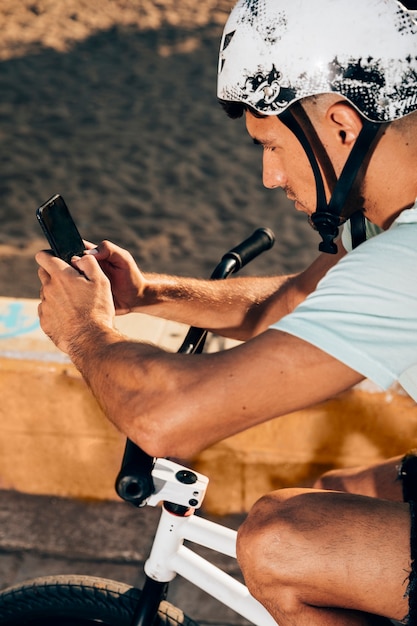 Free photo young man using smart phone on his bike