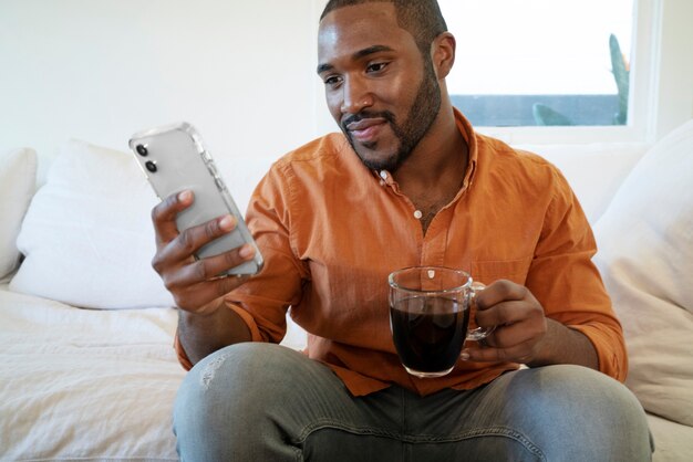 家でコーヒーを飲みながらスマートフォンを使用して若い男