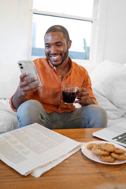 家でコーヒーを飲みながらスマートフォンを使用して若い男