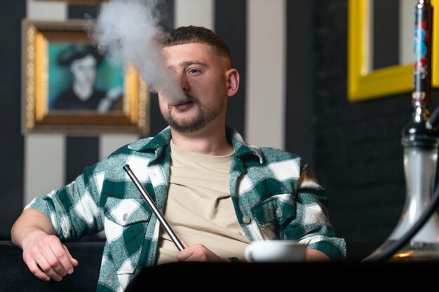 Young man vaping from a hookah in a bar