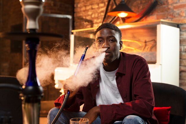 Young man vaping from a hookah in a bar