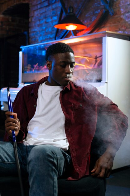 Young man vaping from a hookah in a bar