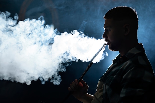 Young man vaping from a hookah in a bar