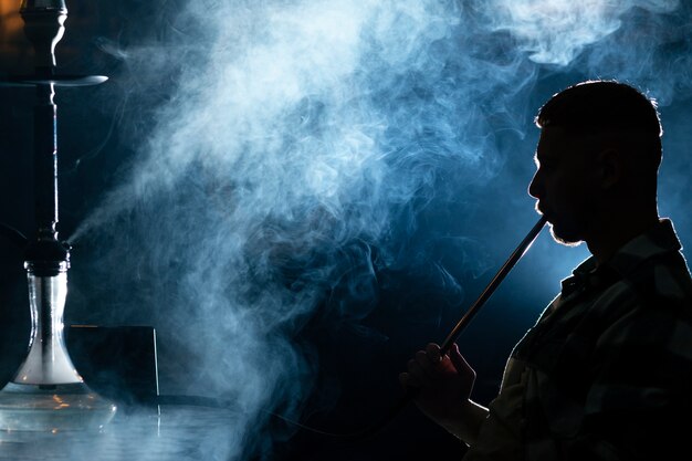Young man vaping from a hookah in a bar
