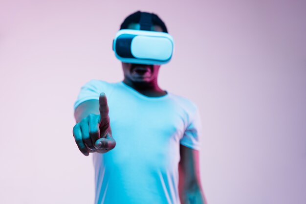Young man in VR-glasses in neon light on gradient