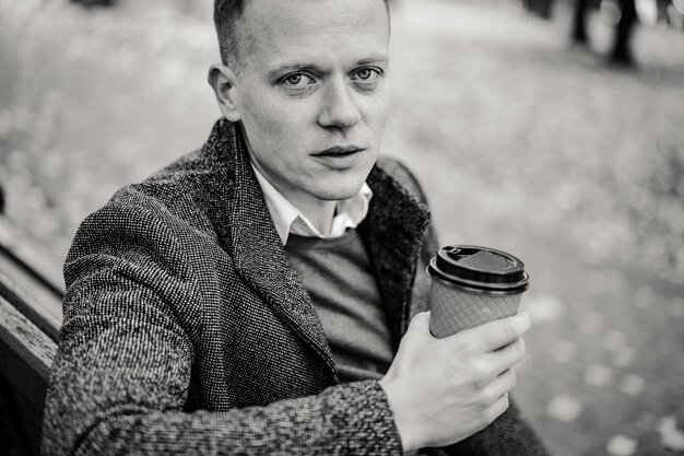 コーヒーを飲みながら秋の街を歩く若い男