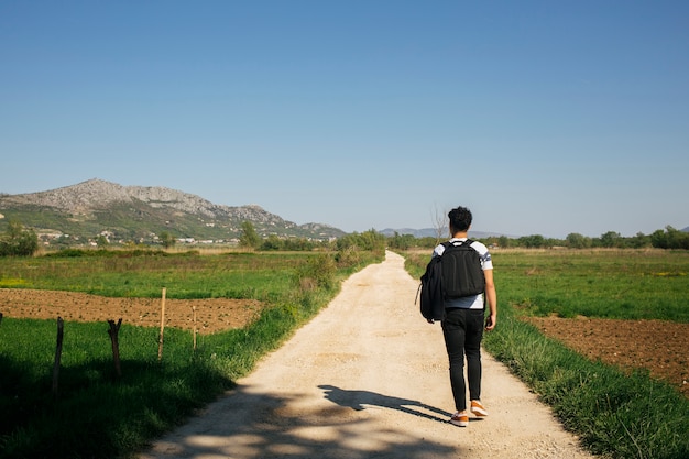 バックパックを運ぶと自然歩道の上を歩く若い男