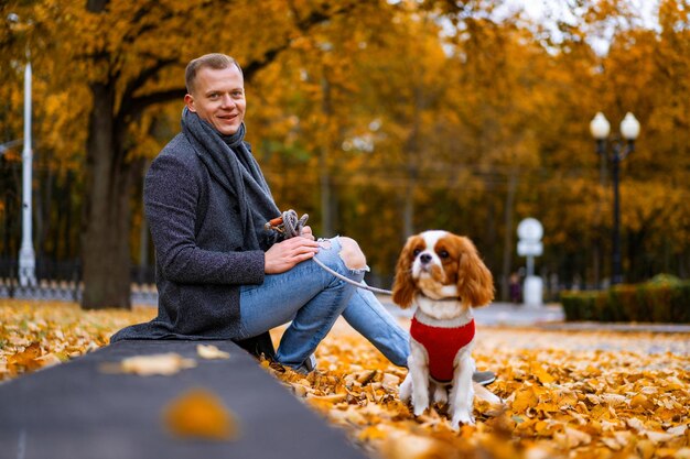 秋の公園で犬と一緒に歩いている若い男
