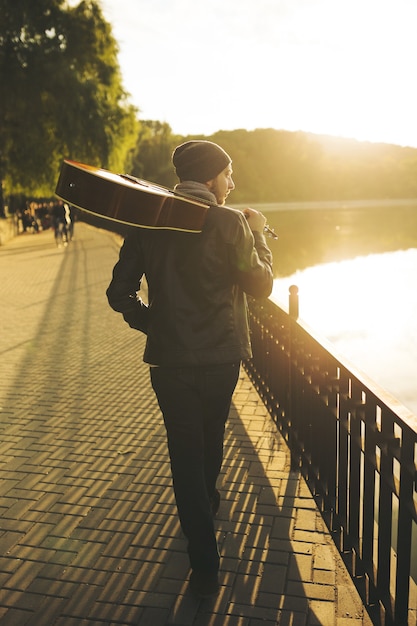 Young man walks by the lake and holding guitar