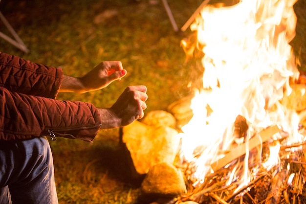 無料写真 焚き火の上で手をウォーミングアップする若い男。山の中のキャンプ場。