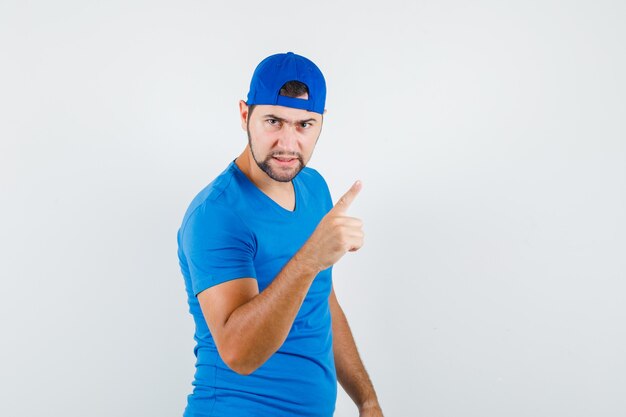 Young man warning with finger in blue t-shirt and cap and looking angry