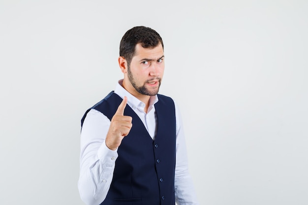 Young man warning with finger in shirt and vest and looking strict