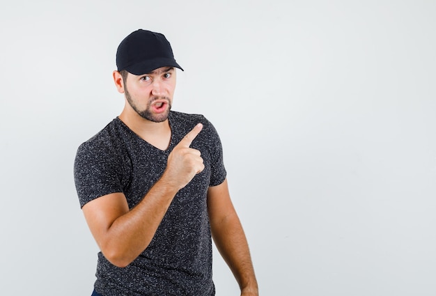 Young man warning with finger in t-shirt and cap and looking serious