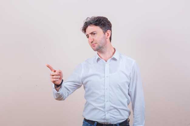 Young man warning with finger in white shirt, jeans and looking strict