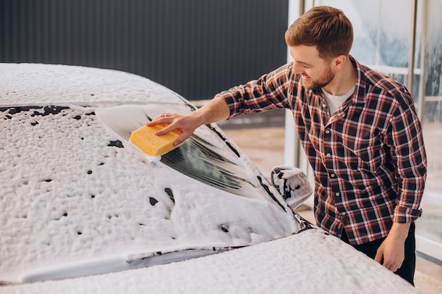 Carwash에서 그의 차를 세척하는 젊은 남자