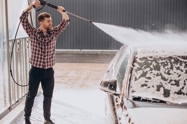 Carwash에서 그의 차를 세척하는 젊은 남자