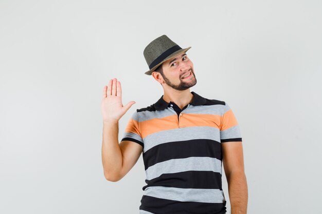 T- 셔츠, 모자에 인사를 위해 손을 흔들며 쾌활한 찾고 젊은 남자