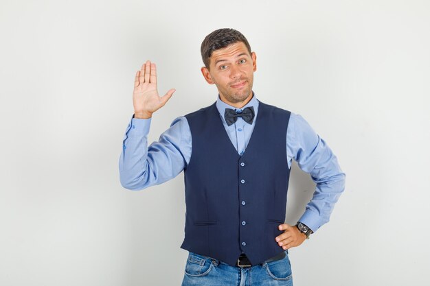 Young man waving hand in hello gesture in suit, jeans and looking cheerful