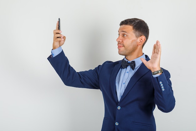 Young man waving hand on videocall in suit and looking cheerful.