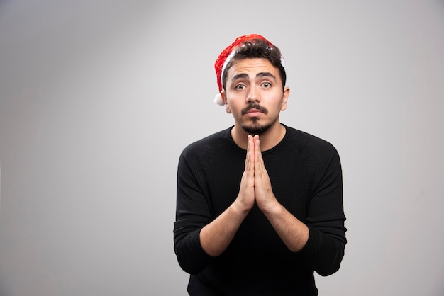 Free photo young man wearing black t-shirt begging with hands together with hope expression on face .