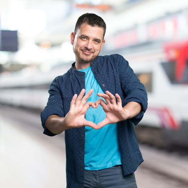 Free photo young man wearing a blue outfit. doing a heart gesture.