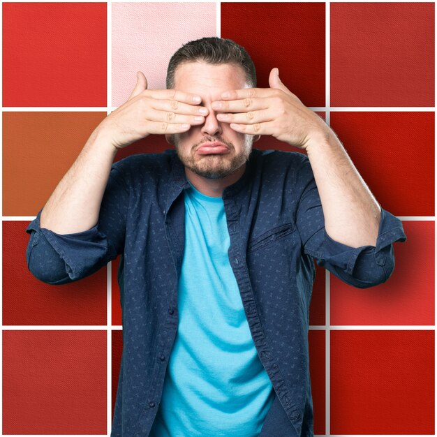 Young man wearing a blue outfit. Sad and covering his eyes with