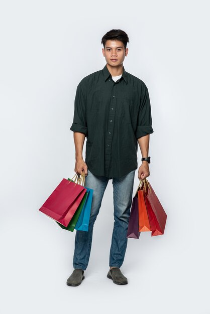 A young man wearing a dark shirt and jeans carries many bags to go shopping