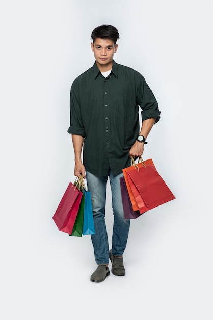 A young man wearing a dark shirt and jeans carries many bags to go shopping