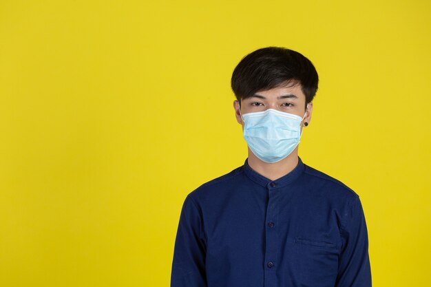 Young man wearing disposable medical mask standing in front of yellow wall